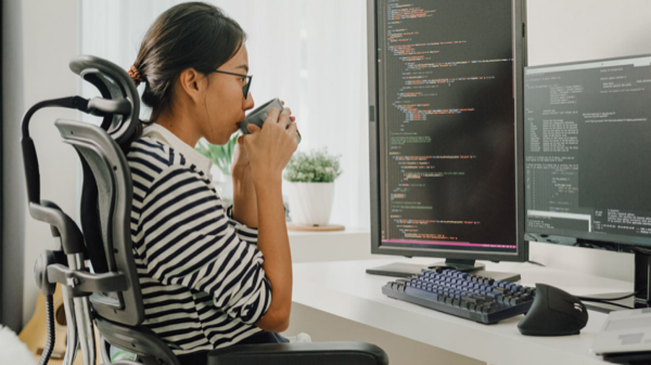 Le développeur buvant du café lors de l’examen du code sur des moniteurs doubles.